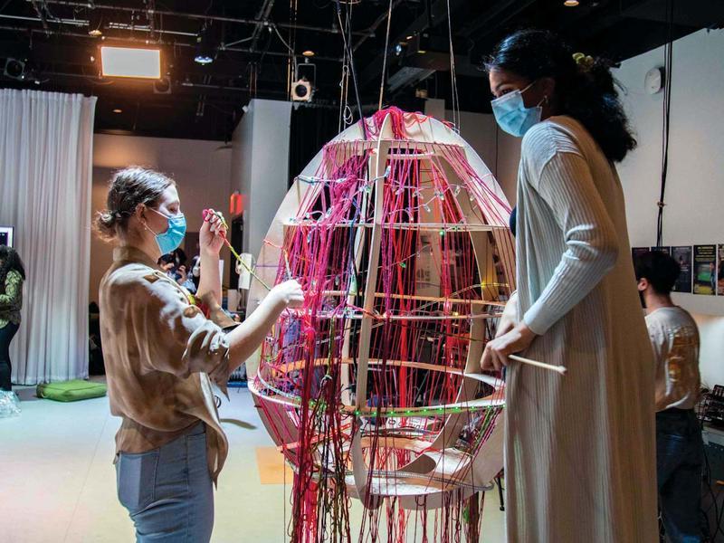2名学生在一个巨大的蛋形物体上编织彩色纱线
